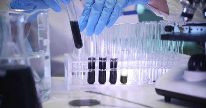 Woman scientist takes test tubes with dark liquid from rack in lab. Technician examines crude oil substances properties in laboratory slow motion