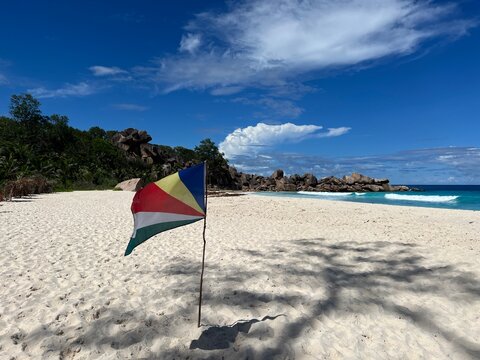 The Seychelles flag on the beautiful Grand Ance beach on La Digue Island in the Seychelles. Turquoise sea, waves, huge cliffs, white sand