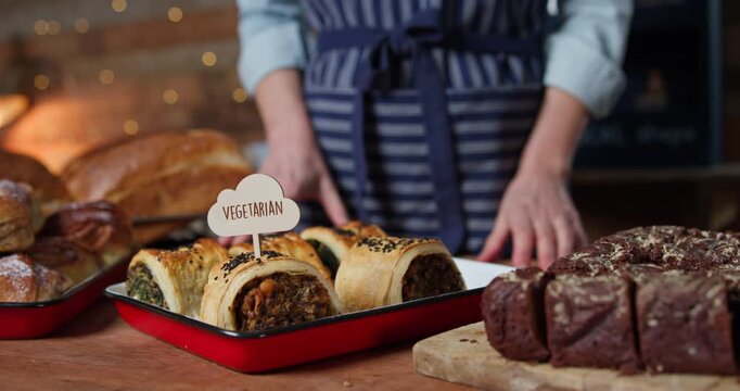 Female Sales Assistant In Bakery Putting Vegetarian Label Into Freshly Baked Baked Savoury Roll