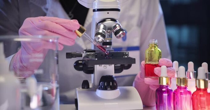 Assistant hand drips serum onto microscope slide in medical lab. Female cosmetologist works on antiaging cosmetic product in laboratory slow motion