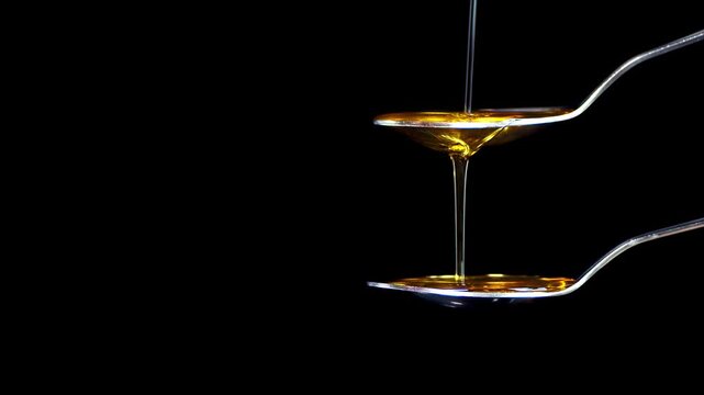 Honey Is Shown Pouring From A Silver Spoon In Slow Motion Against