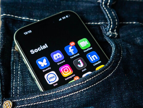 Smartphone inside a dark blue denim jeans pocket displaying social media app icons on the screen
