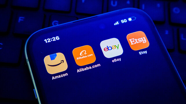 Closeup of a smartphone screen displaying popular ecommerce shopping application icons including amazon, alibaba, ebay, and etsy