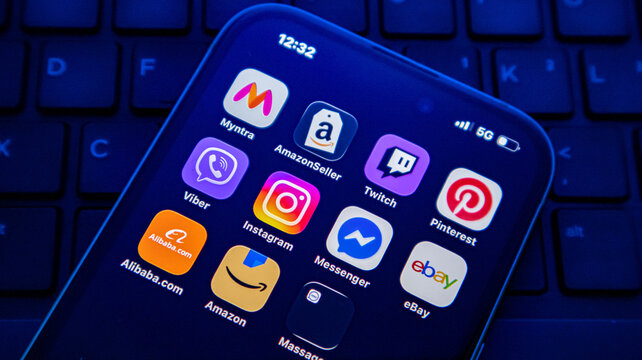 Closeup of a smartphone screen displaying various popular social media and ecommerce application icons on a dark keyboard background