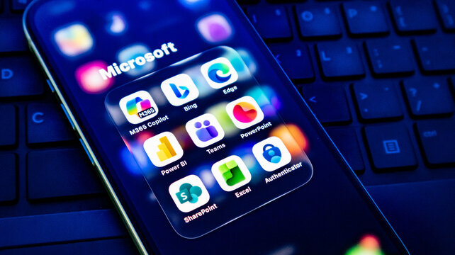 Closeup of a smartphone screen displaying various microsoft application icons including m365 copilot, teams, and powerpoint on a keyboard background