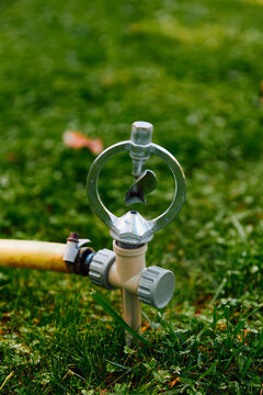 Metal garden sprinkler on a green lawn with a yellow hose