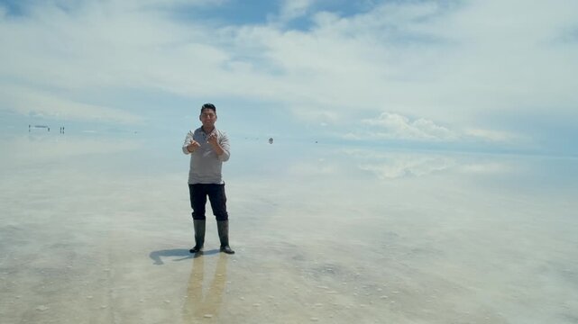A Latino man on vacation at the Uyuni Salt Flats, with the mirror-like effect, inviting people to visit Potos&iacute;, Bolivia - travel concept