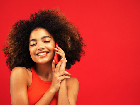 Studio portrait of biracial young woman with red smartphone and afro-textured hair