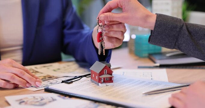 Woman realtor gives key to new house on keychain to customer in agency office. Businesswoman sells real estate to female buyer at company slow motion