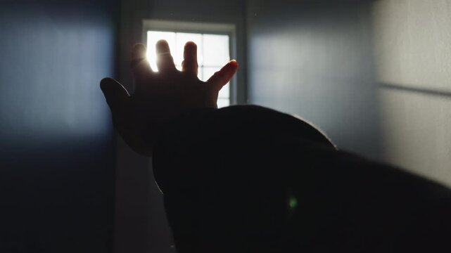 A hand reaches out toward a bright light coming through a door. This happens in the morning when sunlight fills a small room
