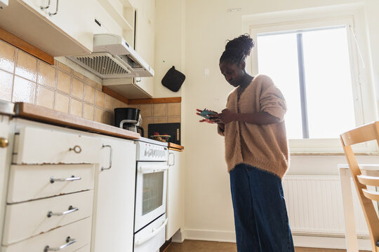 African Woman Using Smartphone While Cooking in White Modern Kitchen