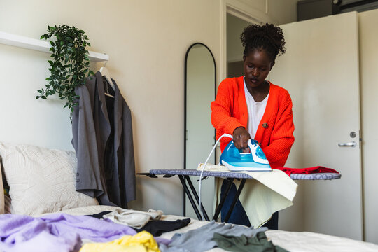Young Black Woman Ironing Laundry on Board in Bedroom