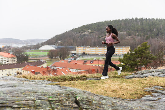 Active Woman Jogging on Rocky Hillside Overlooking City Landscape