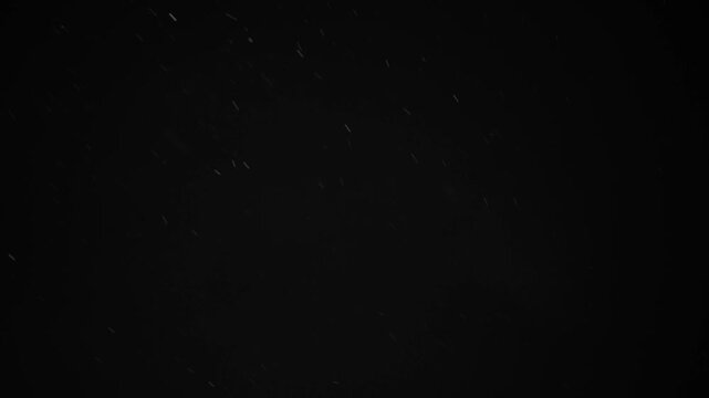 Snowflakes fall gently on a black background during the night. The snowfall creates an atmosphere of winter. Perfect for winter themes and celebrations