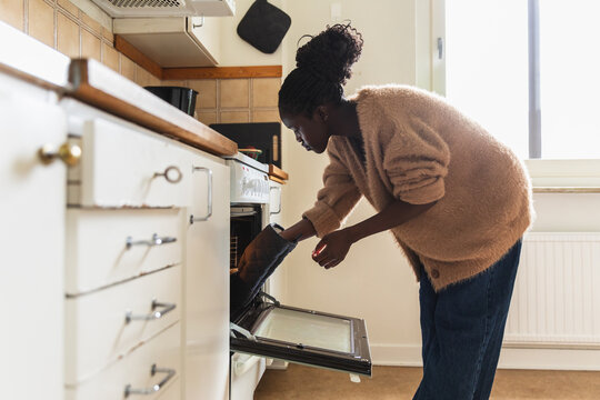 African Woman Putting Baking Tray into Oven in Domestic Kitchen