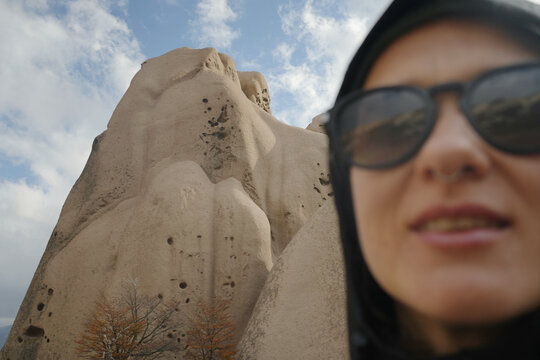 Person Near a Large Rock Formation Under Cloudy Skies