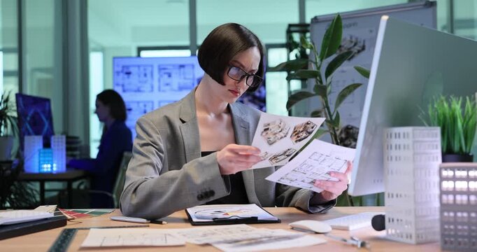 Architect studies detailed documents with building sketches. Woman analyzes complex construction plans and types information into computer slow motion