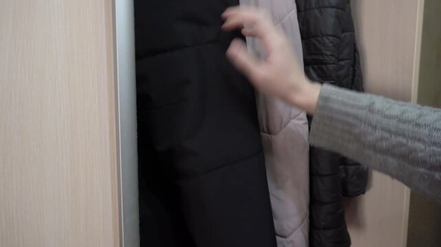 A man chooses a jacket in the wardrobe, A man sorts through warm outerwear hanging on hangers in a home wardrobe. takes clothes from a hanger