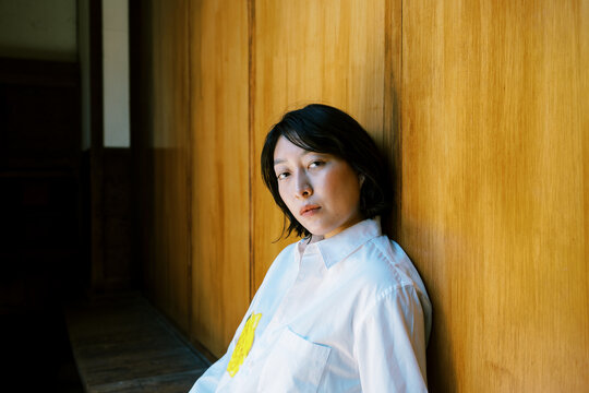 Non-binary person leaning against warm toned wood wall