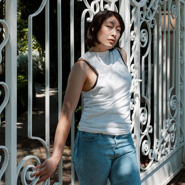 Non-binary model leaning against and holding a white iron gate