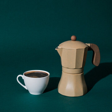 a moka pot and a cup of coffee on a green background