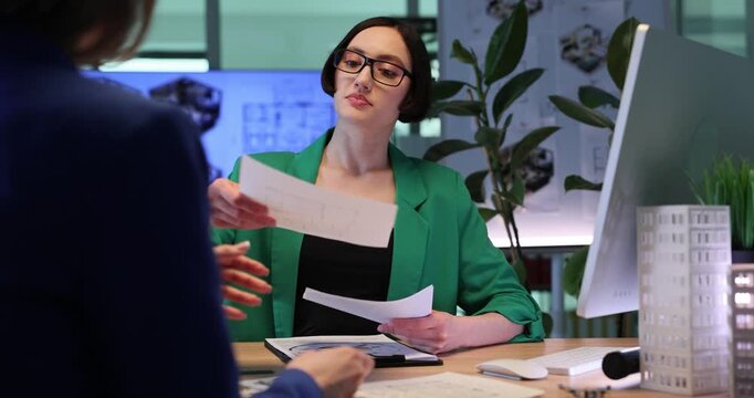Architectural designer shows detailed sketches of buildings to client. Specialist discusses project details with interested client. Slow motion