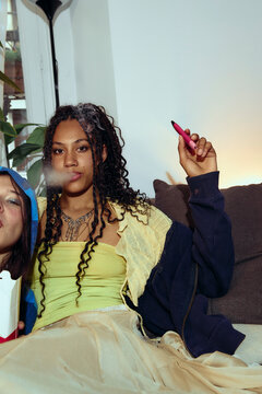 Young woman relaxing with vape at apartment gathering