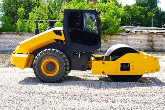 A bright yellow road roller displayed at a construction site. This heavy machinery is positioned on gravel, suitable for industrial use on infrastructure projects and roadworks