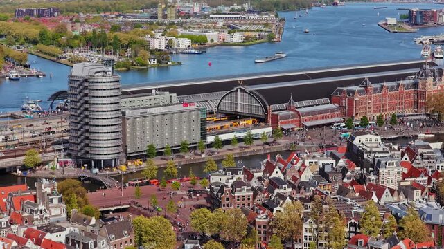 Amsterdam Centraal Station aerial revealing Netherlands historic city architecture and busy water transport on IJ river during a sunny spring day in capital city
