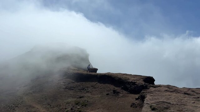 A trekker walking on the edge of the fort with cloud covering him at Harishchandragad.