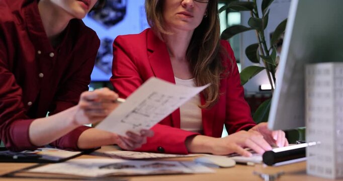 Architectural designers study detailed building sketch. Women examine architectural sketches and enter project data into computer. Slow motion