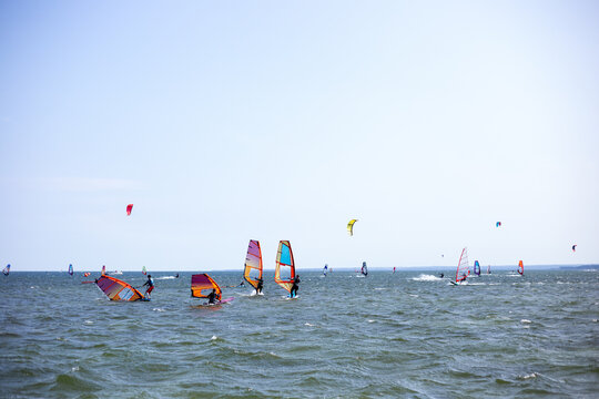 Scenic horizontal view of numerous colorful windsurfing and kitesurfing sails scattered across a glittering sea surface during an outdoor summer sports championship in Chalupy at Hel Peninsula, Poland