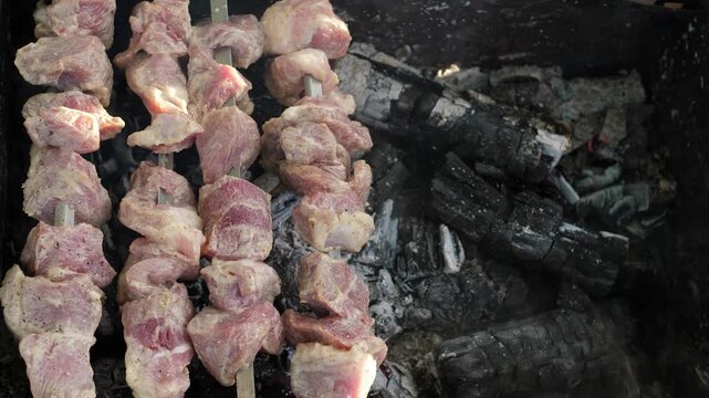 Raw marinated meat on skewers grilling on a mangal, top view. The process of cooking traditional pork shish kebab over hot charcoals with smoke during a picnic.