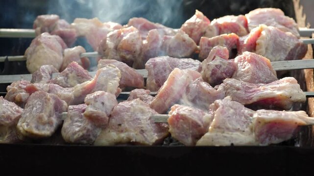 Juicy pork shish kebab close-up grilling on a mangal outdoors. The process of cooking marinated meat on skewers with aromatic white smoke during a summer picnic.