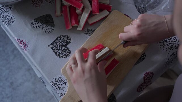 Hands Slicing Surimi Crab Sticks on Wooden Cutting Board