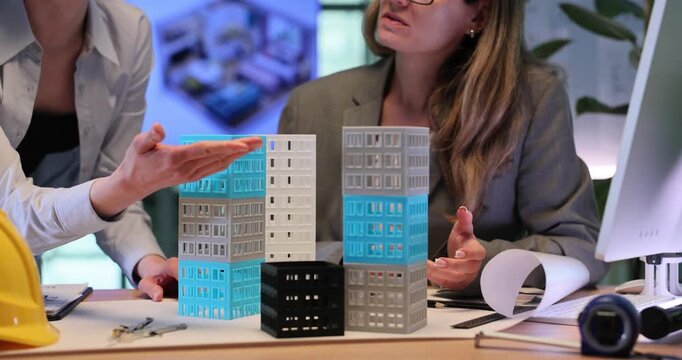 Women examine high-rise building models and analyze design details. Architectural designers discuss creative construction improvements. Slow motion