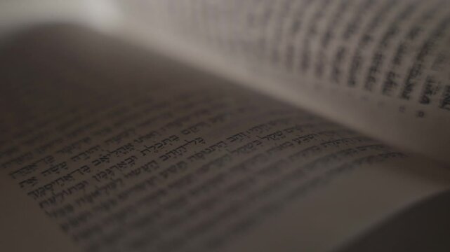 Hand gently traces Hebrew text in open Jewish Bible book of The Old Testament . Soft light illuminates page, evoking quiet focus. Intimate moment of study, reflection, or devotion. Suitable for spirit