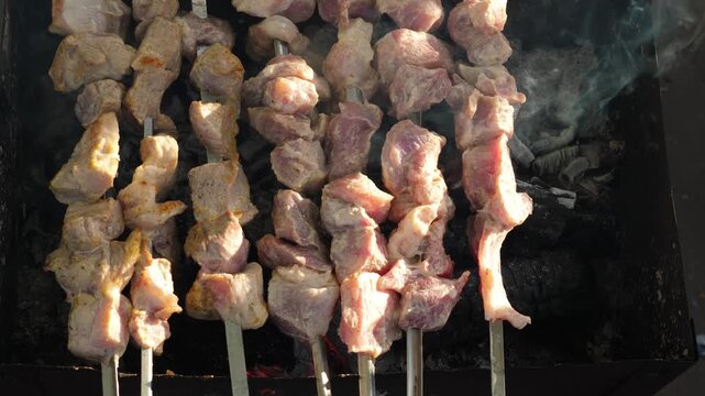 Pork shish kebab on metal skewers grilling on a mangal, top view. The process of cooking marinated meat over hot wood charcoals during a picnic.