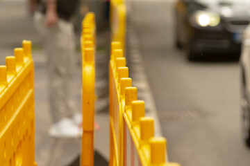 Obraz premium Close-up view of a row of bright yellow temporary plastic barriers lining a city street. Shallow depth of field focuses on the textured barrier posts