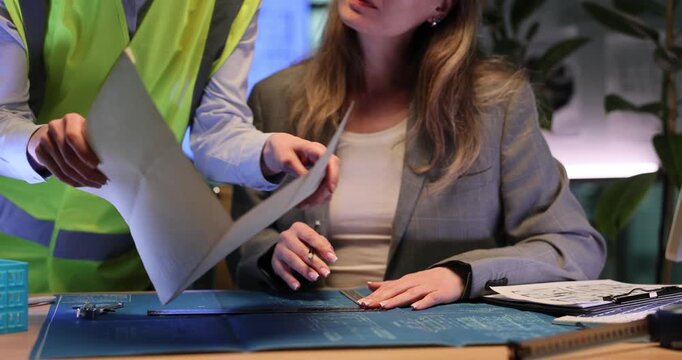 Architect carefully creates detailed building sketch. Woman examines large construction drawings together with experienced builder. Slow motion