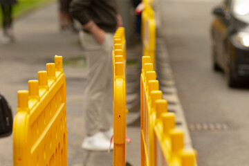 Obraz premium Bright yellow plastic safety barriers form a temporary lane along an urban sidewalk, with shallow depth of field focusing on the nearest barrier and blurred