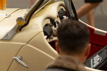 Naklejka premium Rear view of a man leaning into the open cockpit of a cream-colored classic convertible. Visible details include a glossy cream dashboard with chrome trim, a