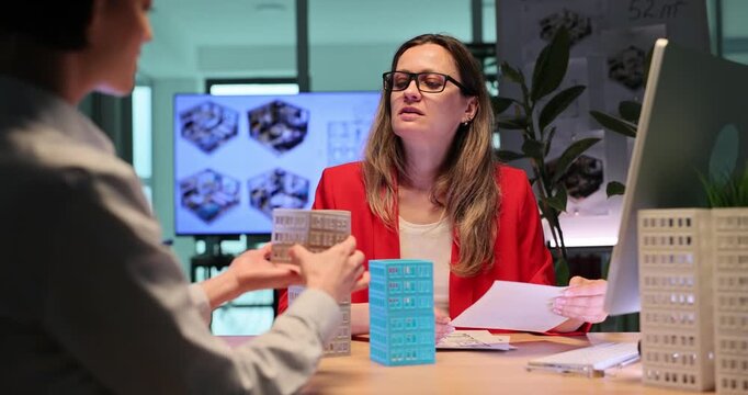 Architects study detailed toy models of multi-story buildings. Businesswomen plan modern construction project in spacious office. Slow motion