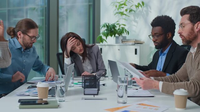Overworked exhausted business team leader boss woman suffer headache group of managers arguing with paperwork at office briefing. Businesswoman stressed with migraine multiethnic workers argue shout