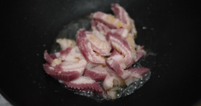 Pieces of juicy pork meat fry in black frying pan. Aromatic steam rises through warm kitchen air. Tender marinated beef sizzles in dark cast-iron pan