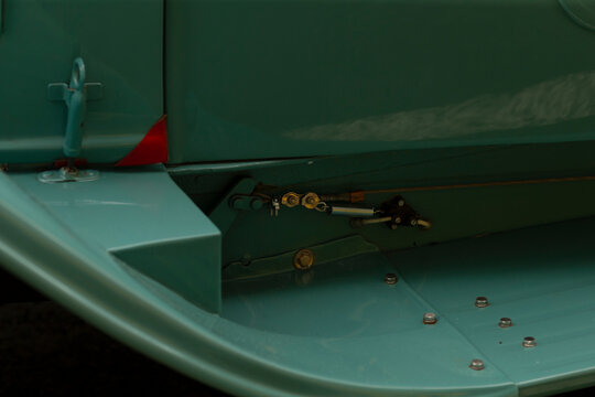 Detailed close-up view of a light green aircraft wing flap area showing metal panels, exposed mechanical linkage, hinge components and flush rivets. Soft