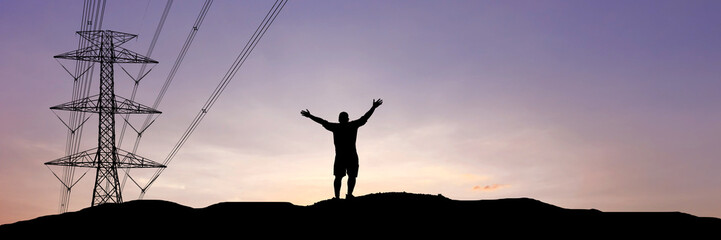 A solitary figure stands silhouetted against a breathtaking sunset, arms raised in triumph beside a towering electricity pylon. ©  2026stockx