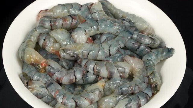 A plate completely full of freshly peeled and headless black tiger shrimp slowly rotating, showing premium seafood preparation.