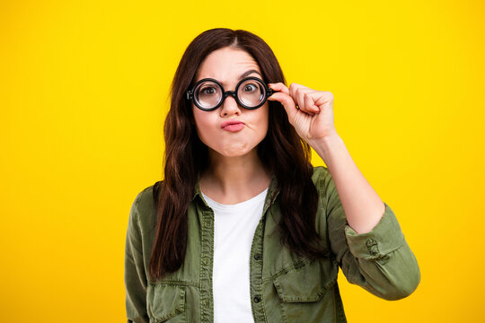Young woman wearing oversized round glasses making a funny confused face against a bright yellow background