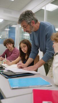 Mature male professor helping teenage students in a high school classroom